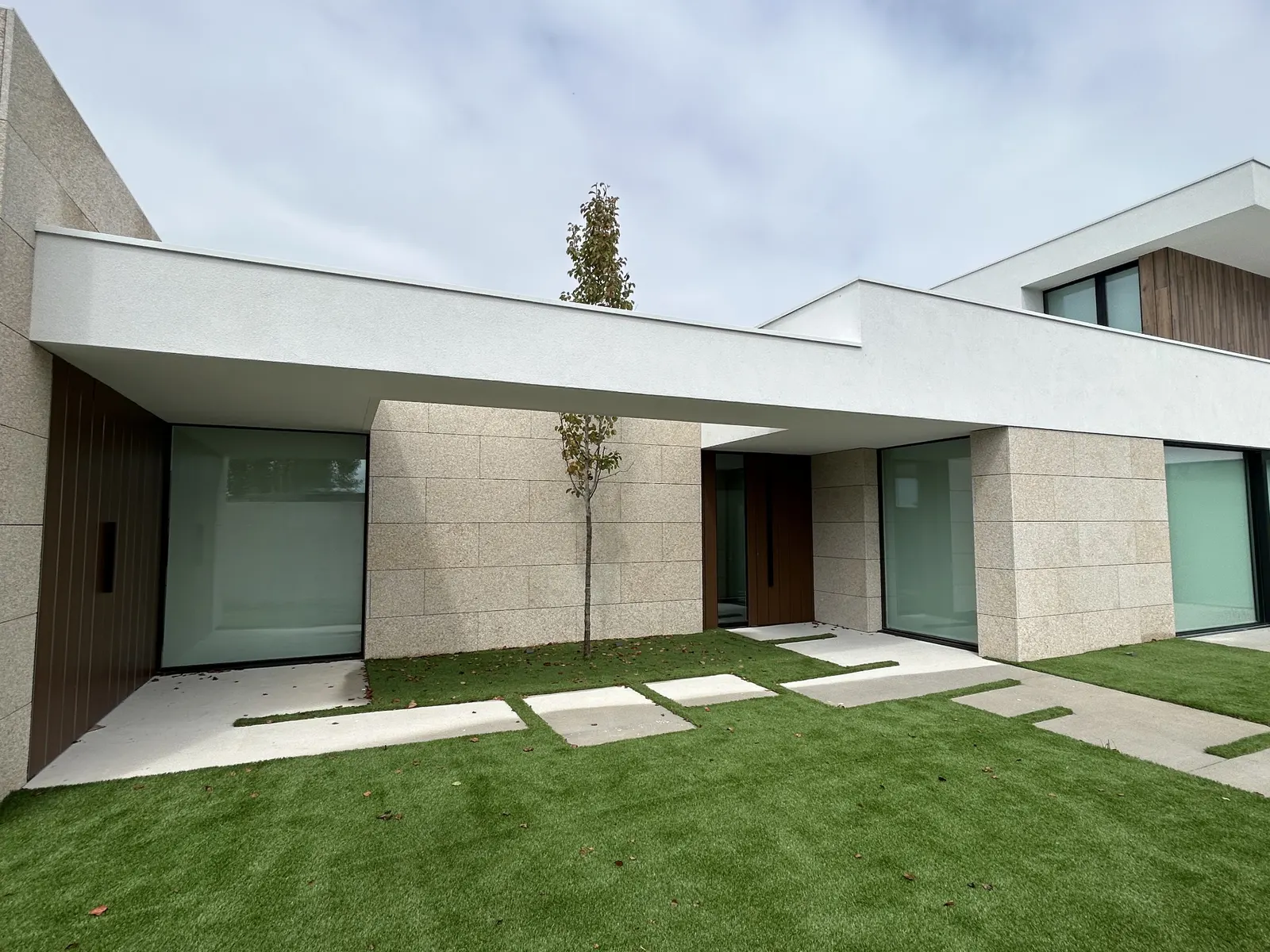 Patio de acceso de vivienda unifamiliar con fachada de granito y puerta de madera